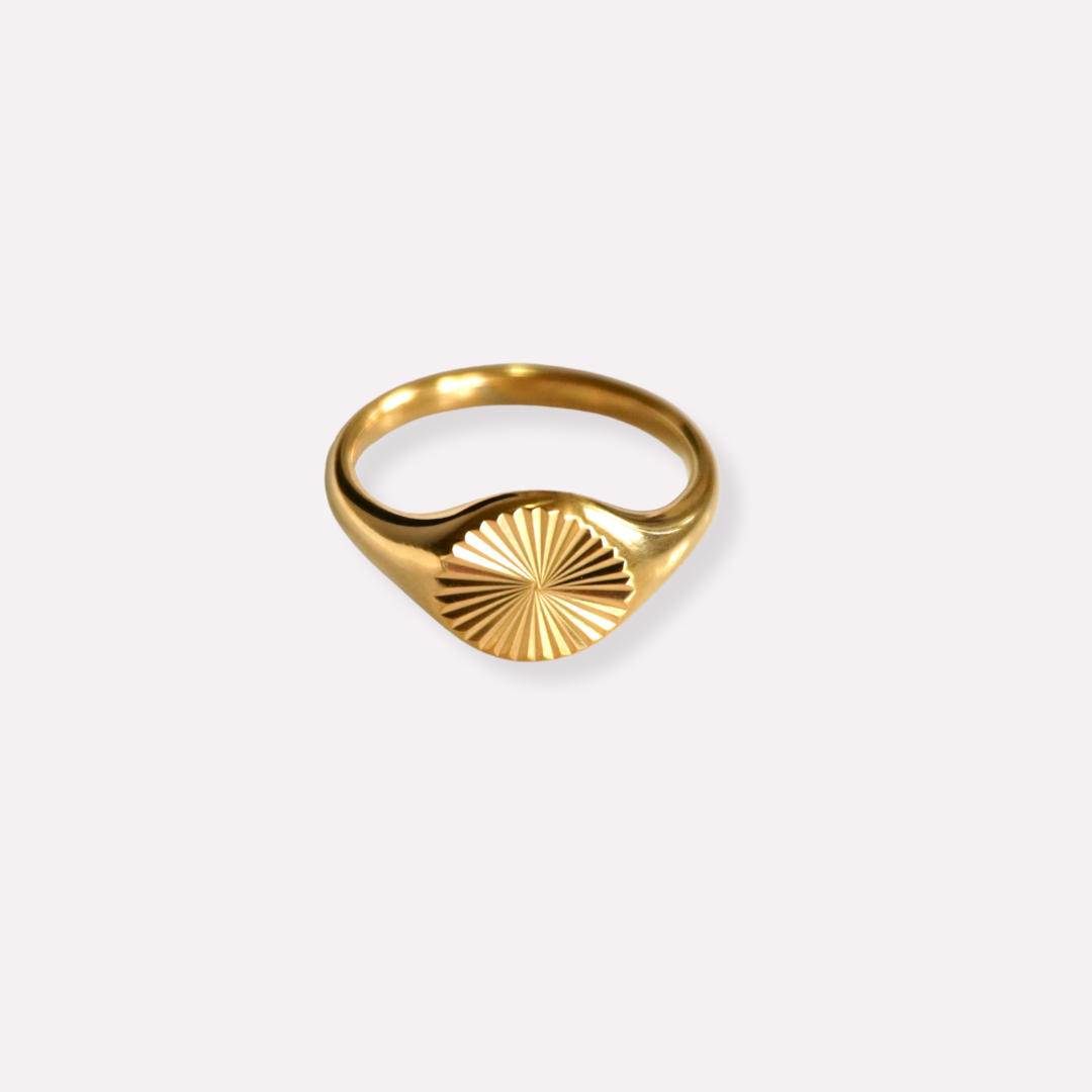 A gold-plated stainless steel signet ring with a sunburst pattern on a plain background.